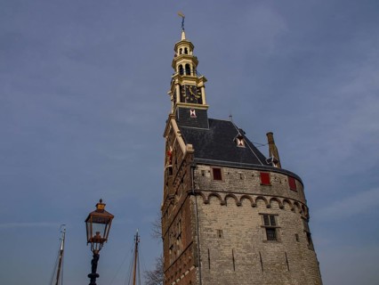 Historic stone clock tower against a sky blue background with an antique lamp in the foreground,