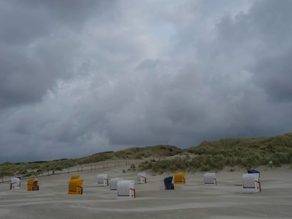 Dune landscape with beach chairs under a grey, stormy sky, colourful beach chairs on the beach and