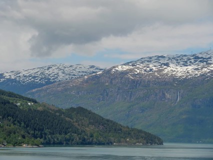 Impressive landscape with snow-capped mountains, a lake and forest under a slightly cloudy sky,