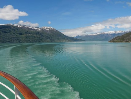 Boat trip on a clear water surrounded by snow-capped mountains and blue sky, greenish shimmering