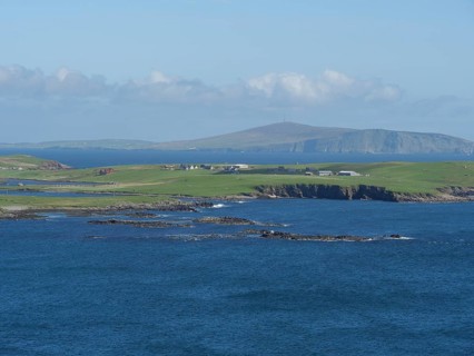 View of the azure blue sea, where green fields reach to the rocky coast, green meadows on a deep