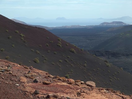 An overgrown volcanic hill with a view of the distant sea under a slightly cloudy sky, barren