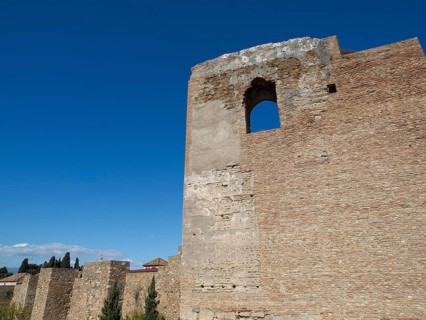 High stone tower with window opening surrounded by blue sky and sunlight, stone walls of an old