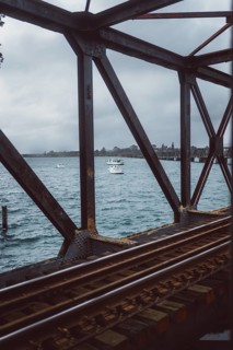 Rusty railway bridge with lake and boats in the background. Cloudy day over Tauranga, New Zealand,