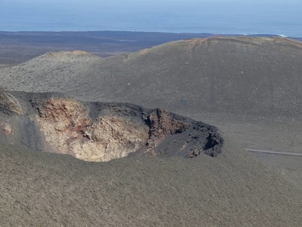 Volcanic crater in a grey desert landscape with a view of the ocean and blue sky, barren landscape
