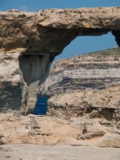 Natural rock arch on the coast, surrounded by rocks and sea under a blue sky, many historic