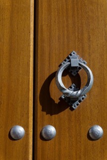 Latch on a wooden door with metal rivets illuminated by sunlight with shadows