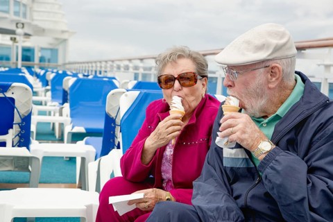Happy senior adult couple enjoying ice cream on the deck of a luxury passenger cruise ship
