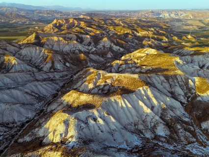 Hilly desert landscape in warm light with deep shadows and clear view of the geographical features,