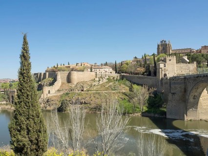 Historic fortress with walls and cypress trees on a hill with river in the foreground on a sunny