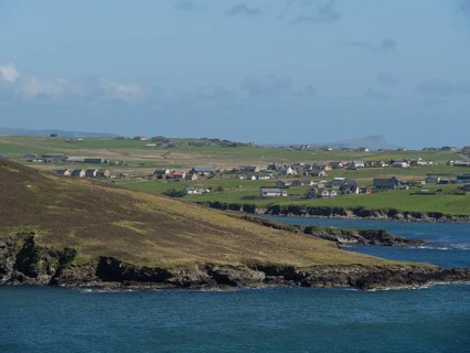 Green hills and houses of a village on a rocky coast with sea view, green meadows on a deep blue