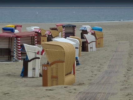 Several beach chairs standing on the sandy shore of a quiet beach with cloudy sky, beach chairs and
