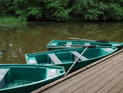Green boats on a wooden jetty on a quiet river with trees in the background, green rowing boats on