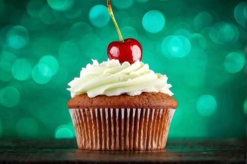 Cupcake with a swirl of vanilla frosting atop a delicate cherry against green background, AI