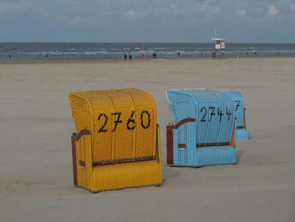 A yellow and a blue beach chair stand close to each other with a view of the sea, colourful beach