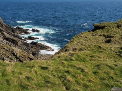Rocky coast with green vegetation and a view of the blue sea, green meadows on a deep blue sea and