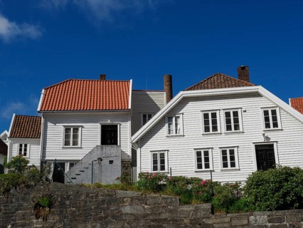 White wooden houses with tiled roofs and chimneys, stone wall in the foreground, sunny day, white