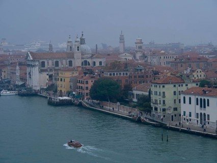 A foggy city view of Venice with historic buildings and boats on the canal, church towers and