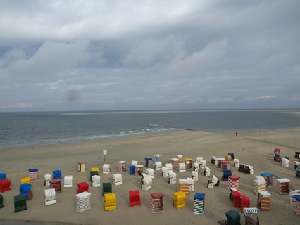 Colourful beach chairs stand abandoned on the beach while the sea and the clouds form the horizon,