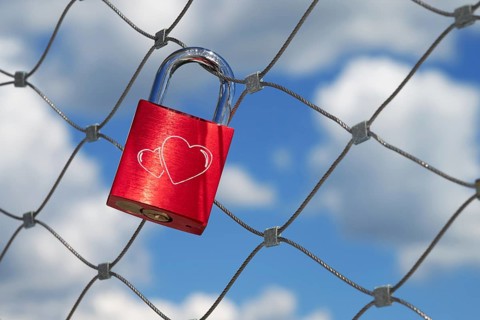 A single red love lock with two engraved hearts hangs from a bridge railing over the Danube,