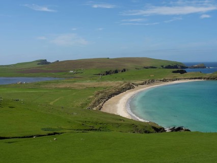 An idyllic coastal scene with rolling green hills, a long sandy beach and calm blue waters under a