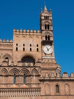Close-up of a cathedral tower with a large clock, under a bright blue sky, two red towers in front