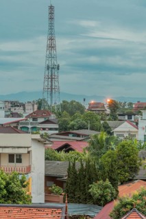 Communication tower above rooftops under cloudy morning sky. Taken from fourth story window in