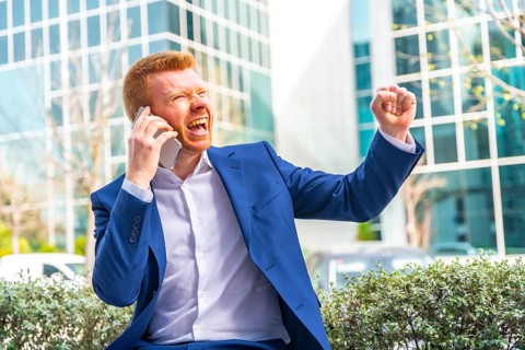 Businessman raising fist celebrating while talking to the mobile sitting in the city