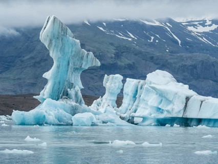 A majestic iceberg forms a breathtaking sculpture surrounded by water with mountains in the