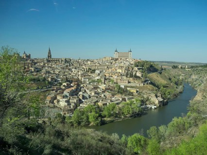 View of a historic riverside town with distinctive church towers and bridges, framed by hills under