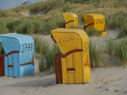 Colourful beach chairs standing on the sandy beach, surrounded by green dunes and a cloudy sky,
