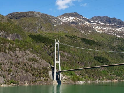 Bridge spanning forested mountains and a green lake, under a clear blue sky, bridge in a fjord with