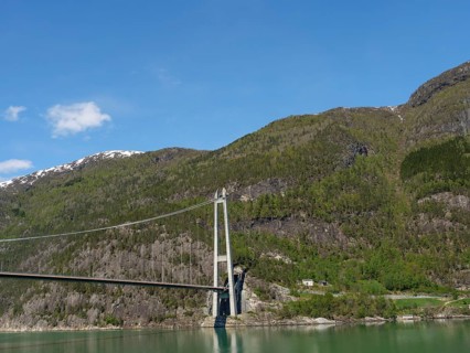 Wide angle view of a bridge over green mountain slopes and forests under a clear blue sky, bridge