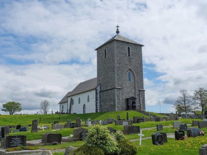 Stone church on a hill surrounded by a cemetery with numerous gravestones under a cloudy sky, old