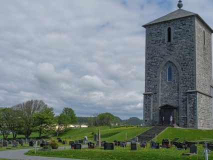 Stone church and cemetery with numerous gravestones under a cloudy sky in a rural setting, old