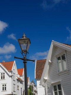 Street lamp in front of white houses with red roofs under blue sky with clouds, white wooden houses