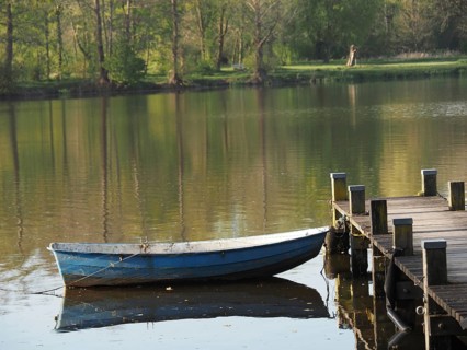 A boat is moored to a jetty and reflected in the calm waters of a lake, rowing boats and pedal