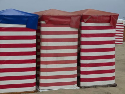Three colourful beach huts with striped pattern stand on the sandy beach, beach chairs and beach