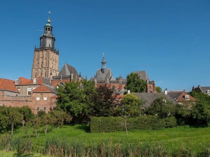 Historic church with a bell tower, surrounded by brick buildings and a green park under a clear