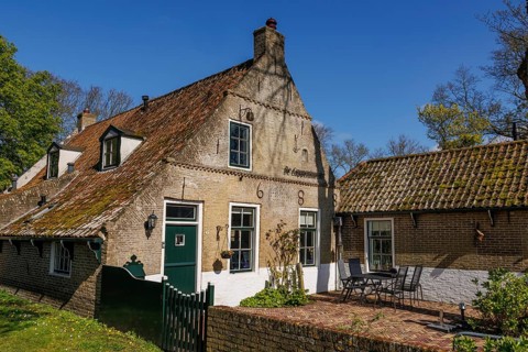 An old house with tiled roof and terrace, surrounded by green plants on a sunny day, historic