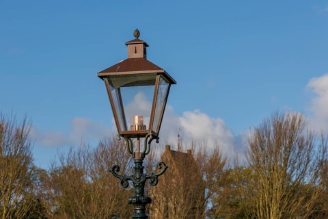 Classic street lamp against a clear blue sky and bare trees in the background, old houses and small
