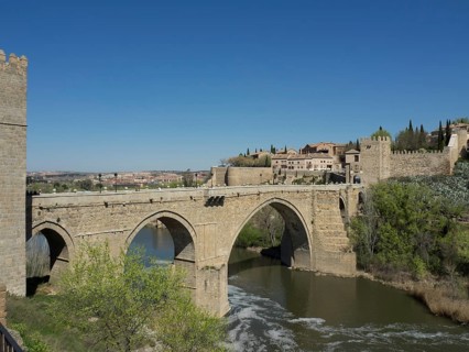 Historic stone bridge over a river surrounded by a city and nature, blue sky in the background,