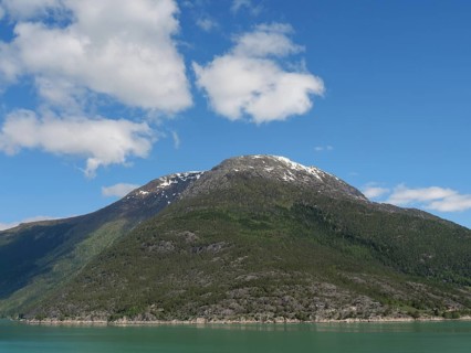 Majestic mountain with snow-covered peak and lake below under a clear sky, greenish shimmering