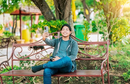 Relaxed guy taking a selfie sitting on a bench at sunset. Smiling man sitting on a bench taking a