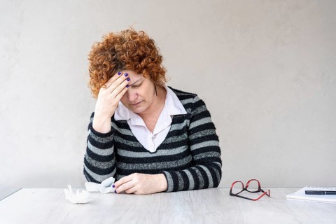 A mid-adult redhead woman is holding one hand on her forehead