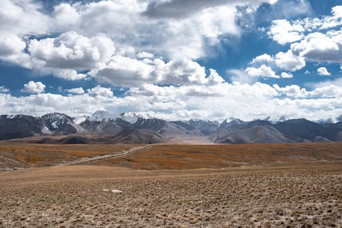 Car on a gravel track in the high mountain plateau, glaciated and snow-covered peaks, Ak Shyrak