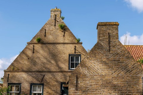 Traditional brick house with windows and chimney in front of a blue sky and scattered clouds,