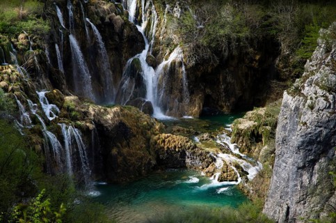 A picturesque waterfall that pours over rocks into crystal-clear water, surrounded by lush green