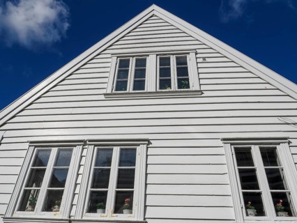 Close-up of a white wooden house with several windows in front of a blue sky, white wooden houses