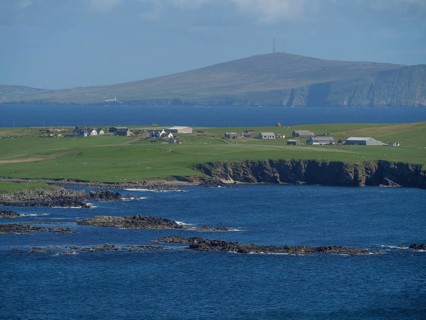 Coastal landscape with houses on green hills and blue ocean in the background, green meadows on a